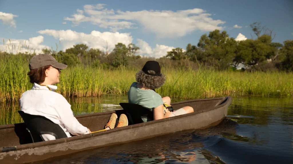 Guests enjoy a relaxing mokoro safari in Khwai, Okavango Delta, surrounded by lush greenery and peaceful waters.
