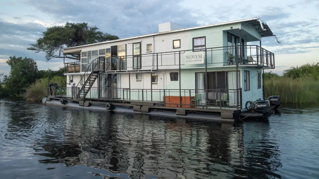 Ngwesi Houseboat floating on the waters of the Okavango Delta, Botswana, with lush greenery in the background.