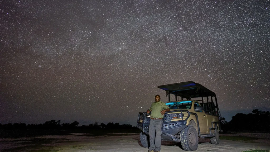 Safari guide standing beside game vehicle under a star-filled sky during a night drive in Khwai, Botswana â€“ unforgettable stargazing and nocturnal wildlife experience.