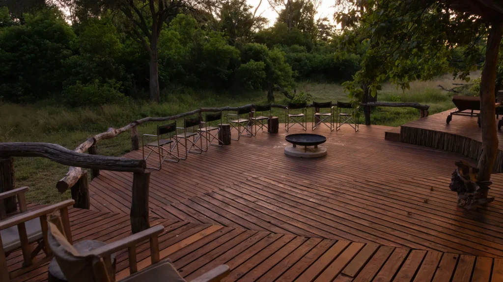 O Bona Moremi Safari Lodge's wooden terrace with seating arranged around a fire pit, set amidst lush greenery in the Okavango Delta.