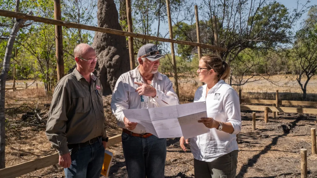 O Bona Moremi construction team discussing building plans at the Okavango Delta site with a focus on the blueprint and ongoing development.